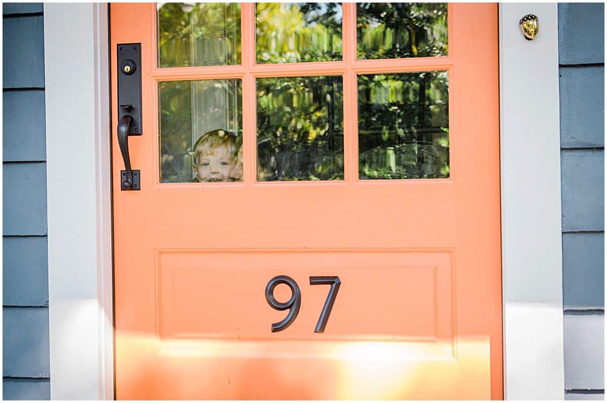 mom and son are peeking from the window of their orange front door in Montclair NJ