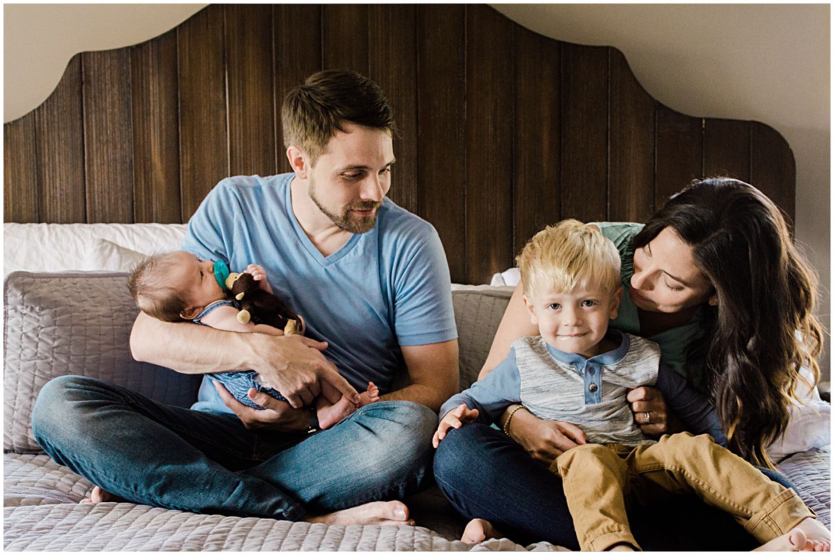 family is cozy on bed with mom snuggling with her son and daddy holding his baby girl at their NJ home