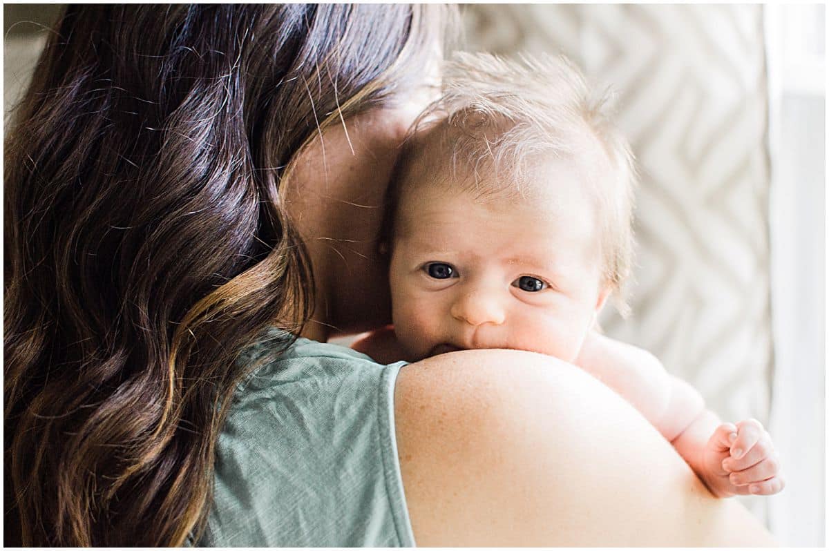 awake newborn baby peeks over the shoulder of her mom in newborn photography portraits