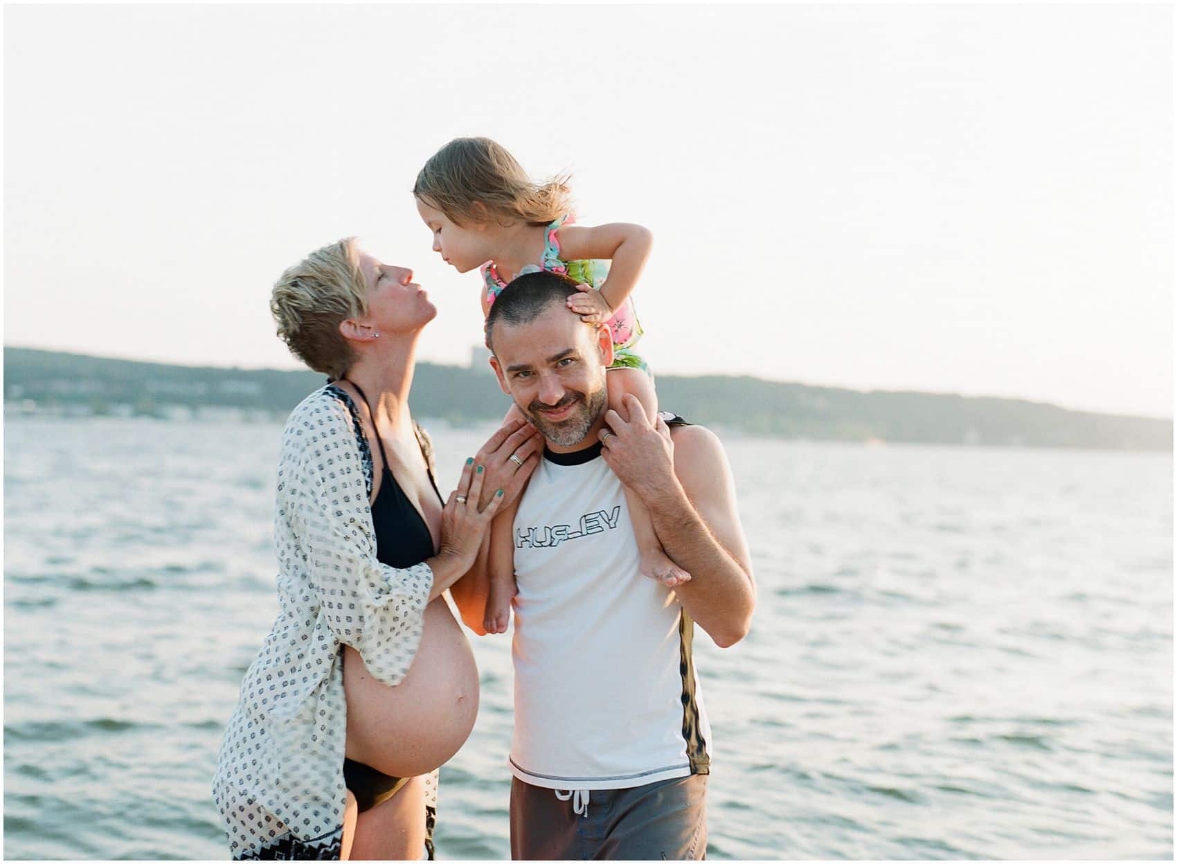 pregnant mom kissing her daughter at the beach and father is smiling