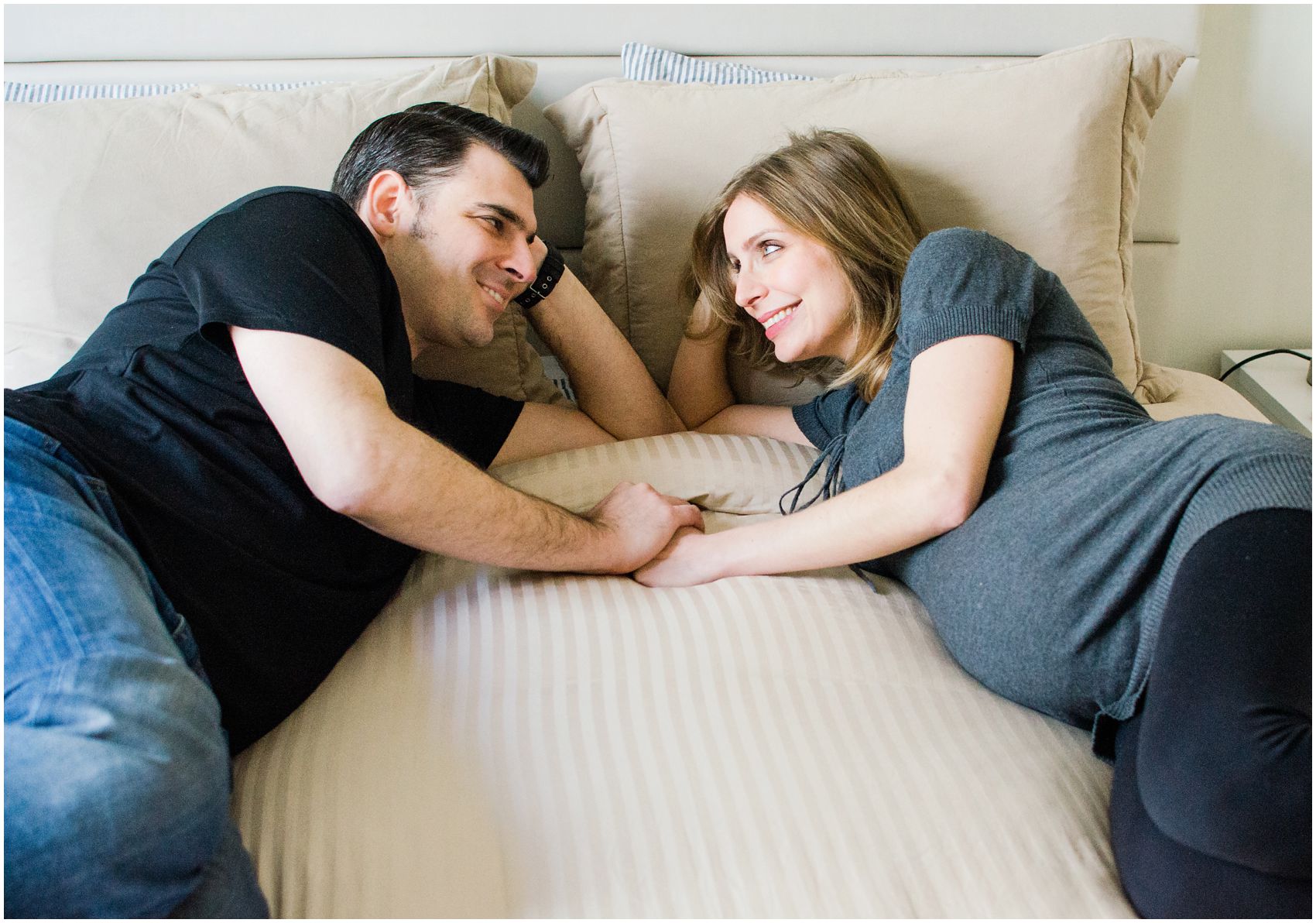 pregnant couple laying in bed and looking at each other