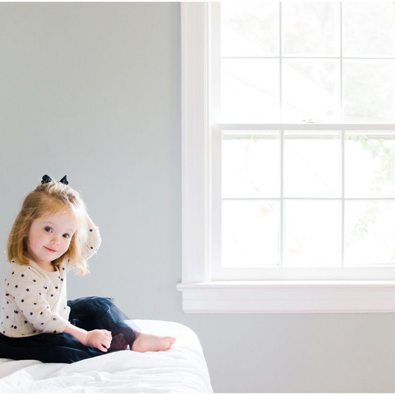 Little girl sitting by the window on her bed in Montclair NJ, captured in a beautiful family photography moment