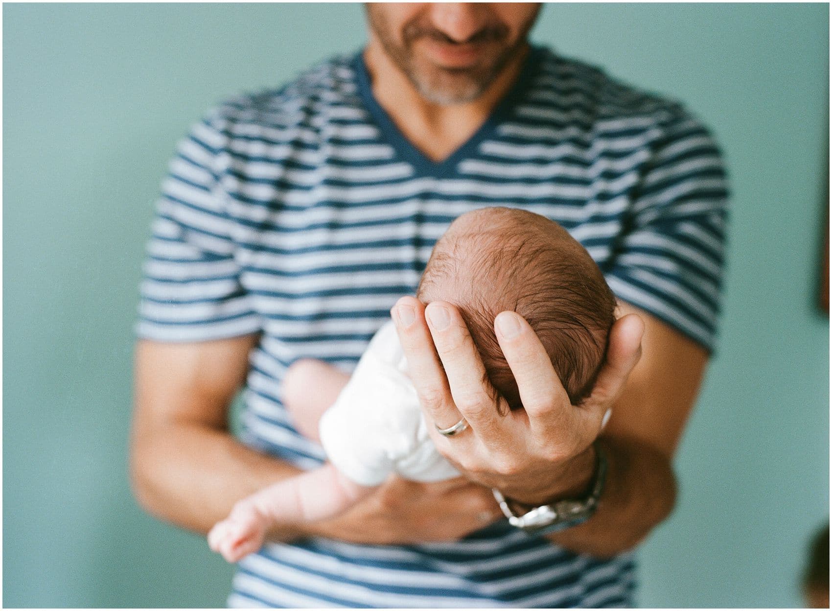 a close up of small baby head in loving hands of the dad