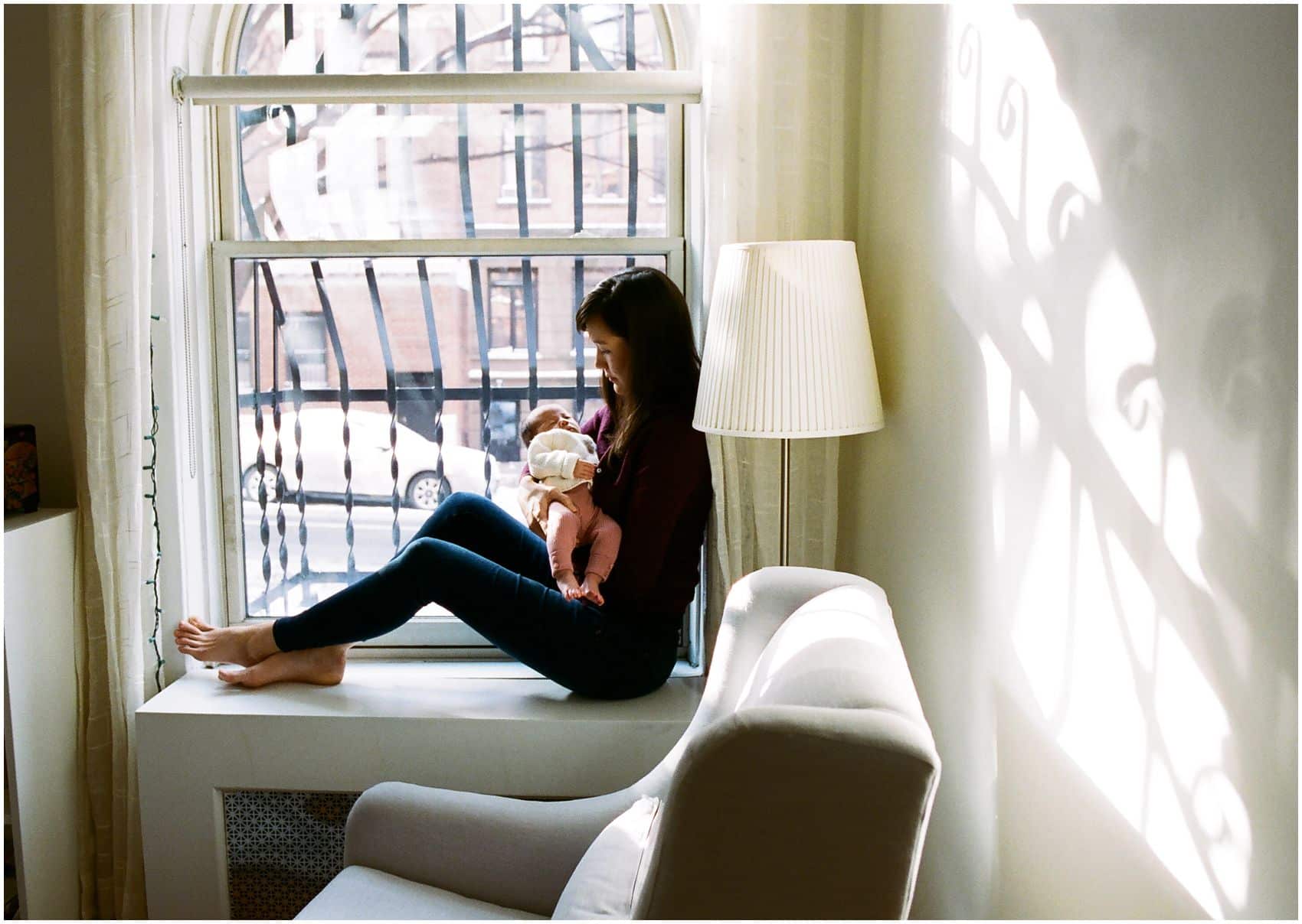 NYC Newborn Photographer Miriam Dubinsky shares tips on when is the best time to schedule the newborn photos mom holding baby girl by the window