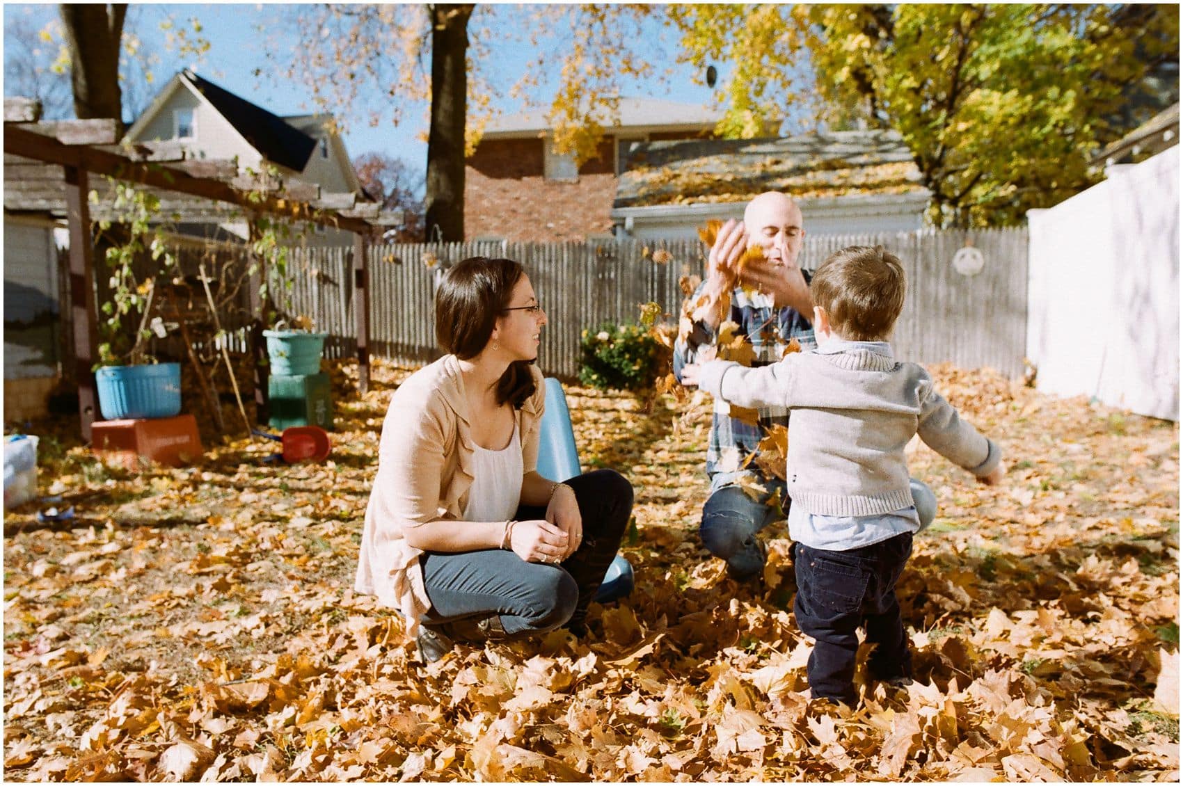 fun family photo of parents playing with yellow leaves with their son during fall season in their NY backyard