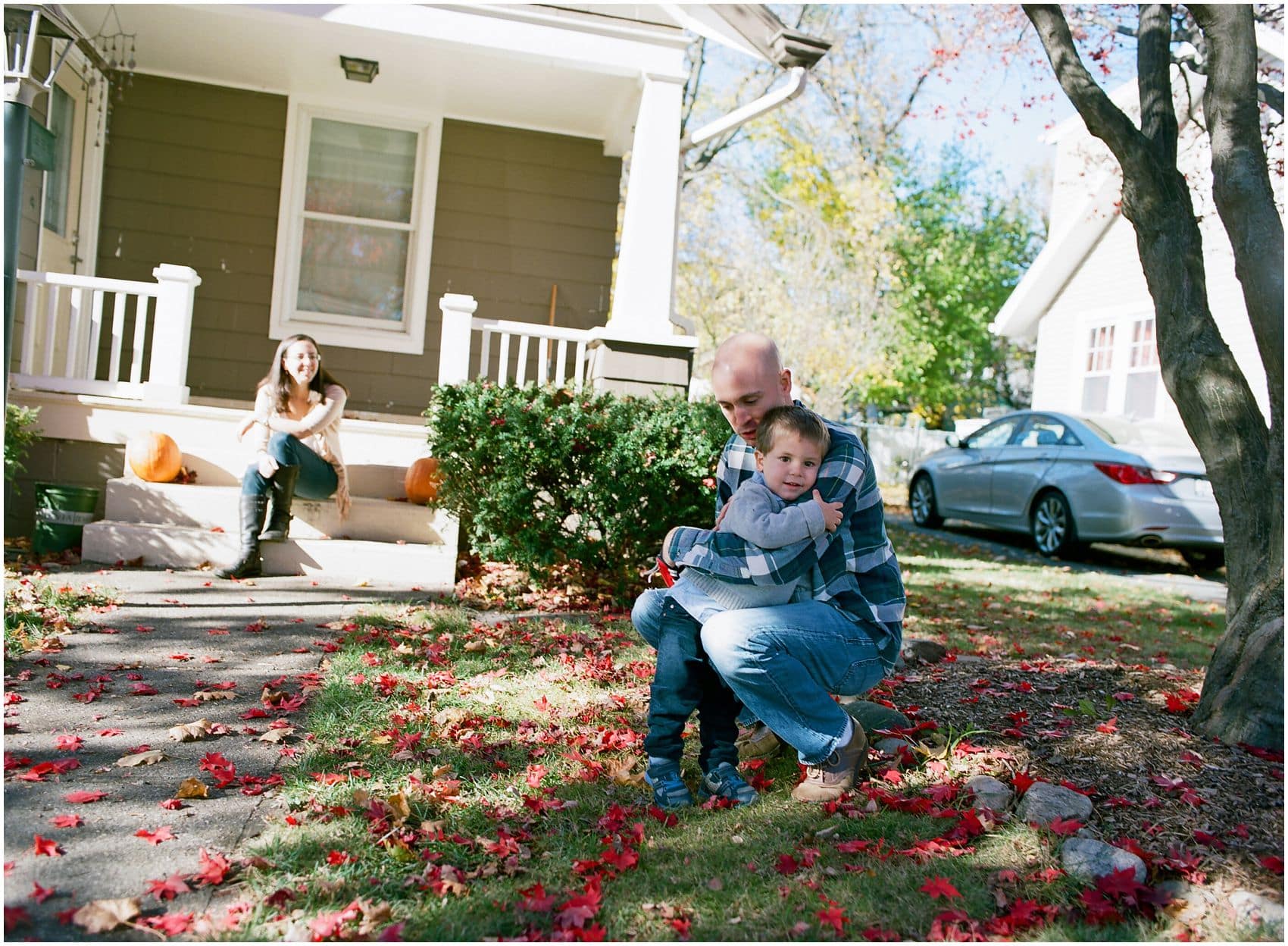 Dad hugging his little boy in front of his home during family portraits fall season