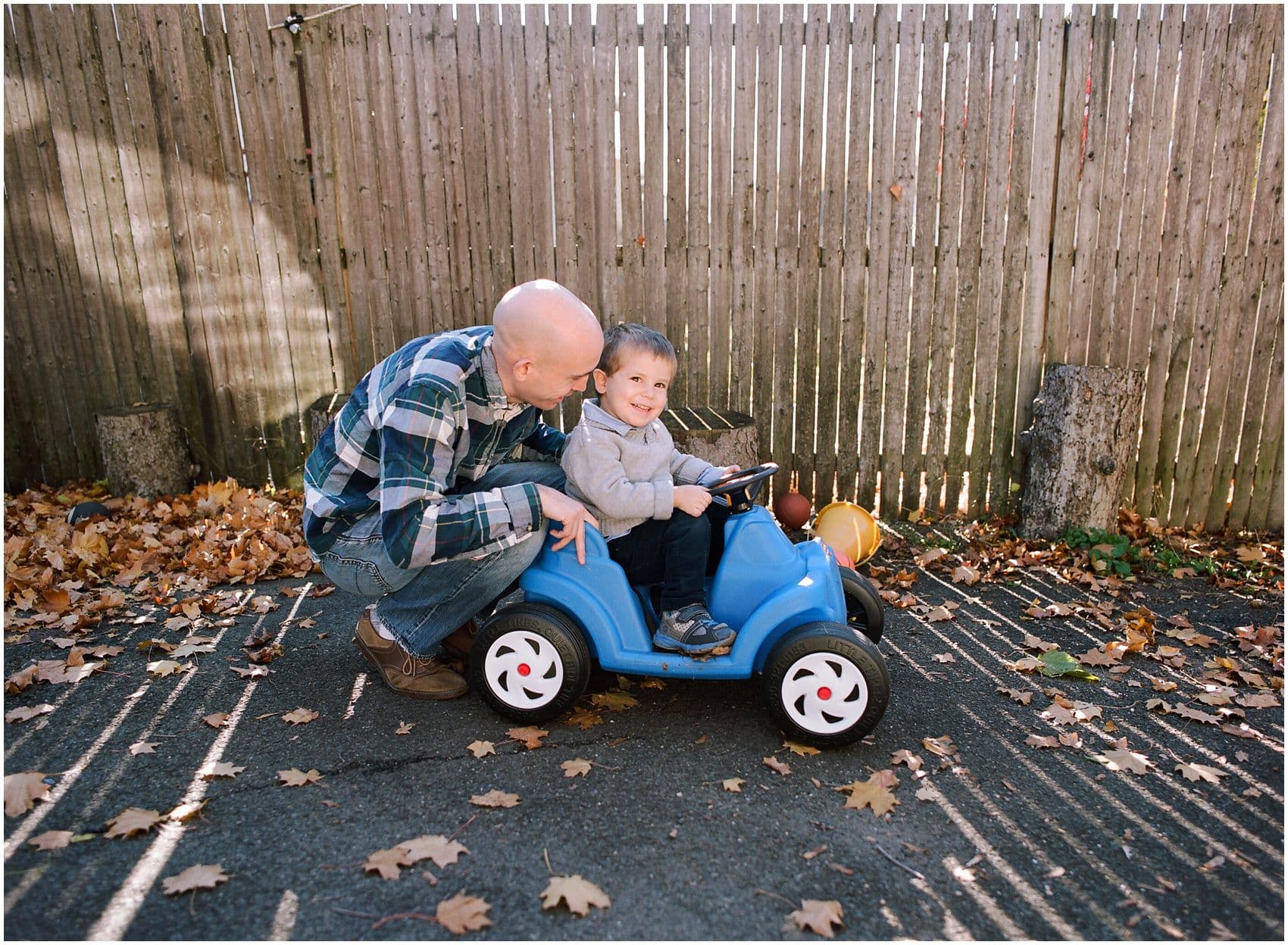 dad pushing his little boy in a blue car surrounded by fall yellow leaves in Rockland County