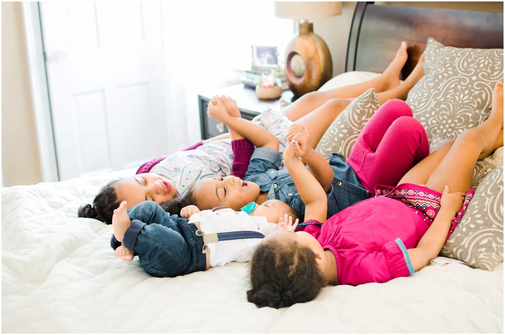 siblings laying on the bed and holding hands during NJ family portraits 