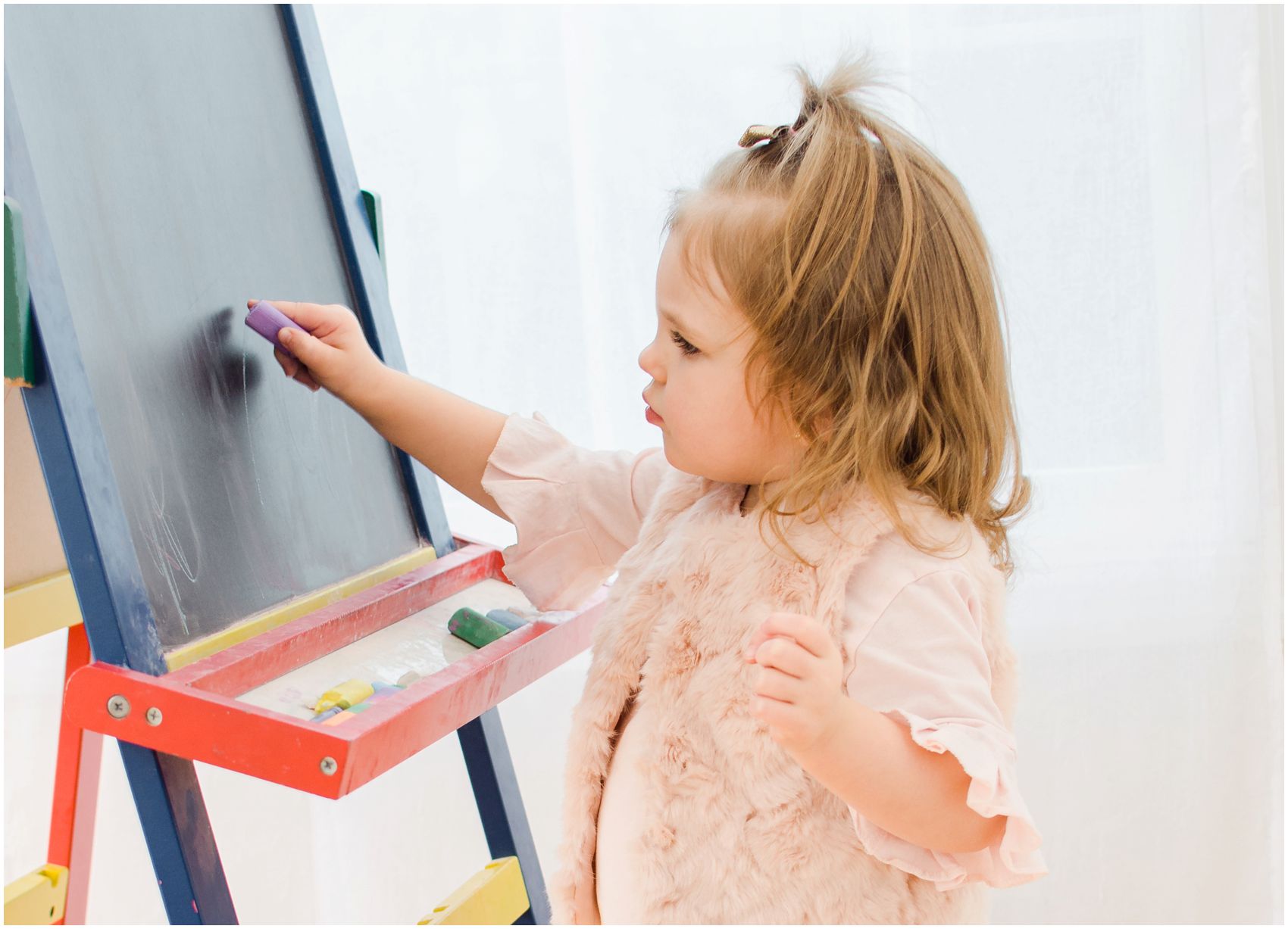little girl with a ponytail drawing on the easel board during her Mommy and Me Lifestyle Session