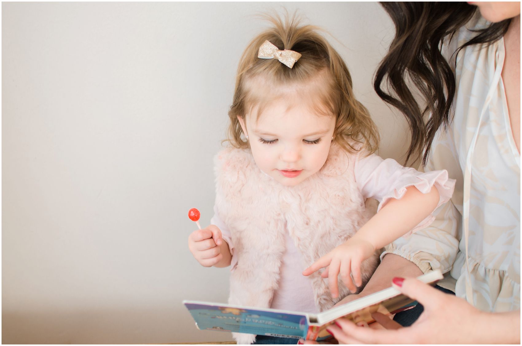 little girl eating a red candy and reading a book with her mom in family photography NYC