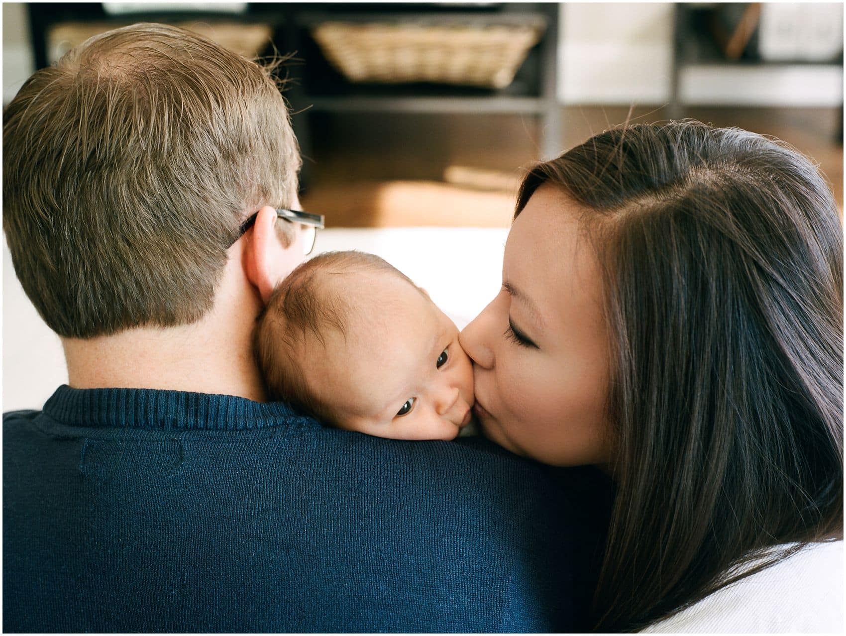 mom and dad kiss and squish their baby cheeks in a newborn portrait 
