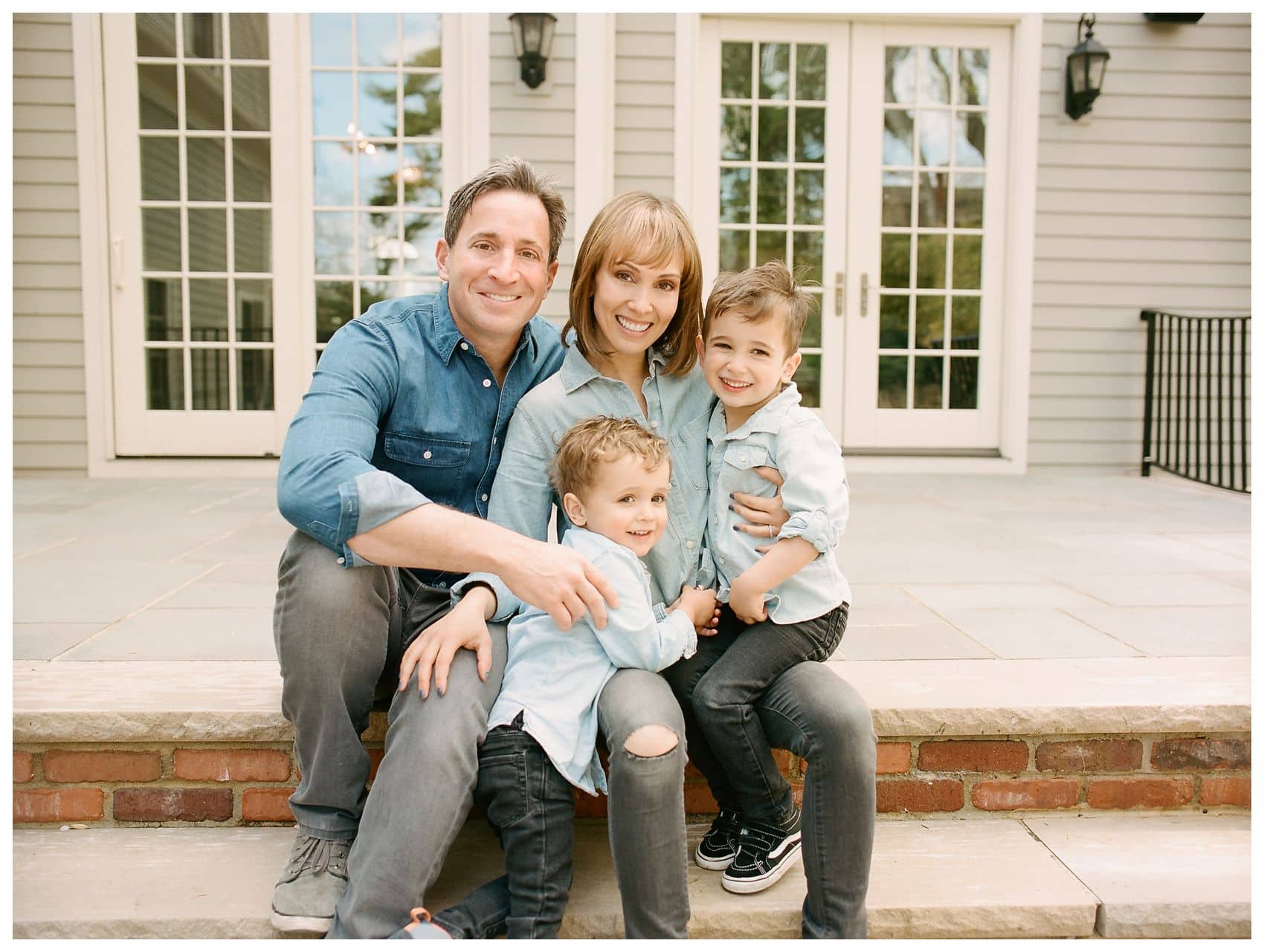 family photography of a family of 4 with two little boys sitting on their porch wearing denim jeans in Essex County