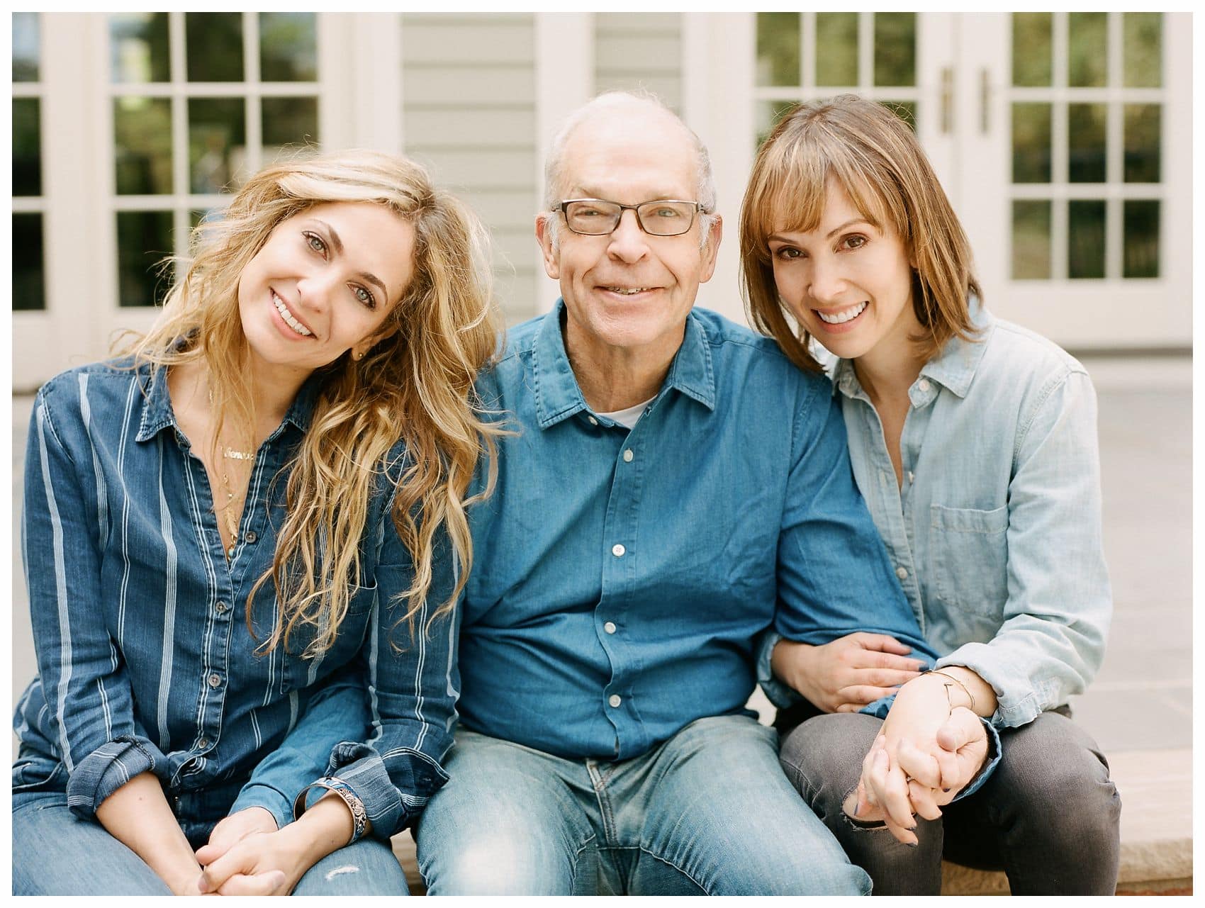 dad sitting with two adult daughters in front of their home in NJ wearing all blue denim colors