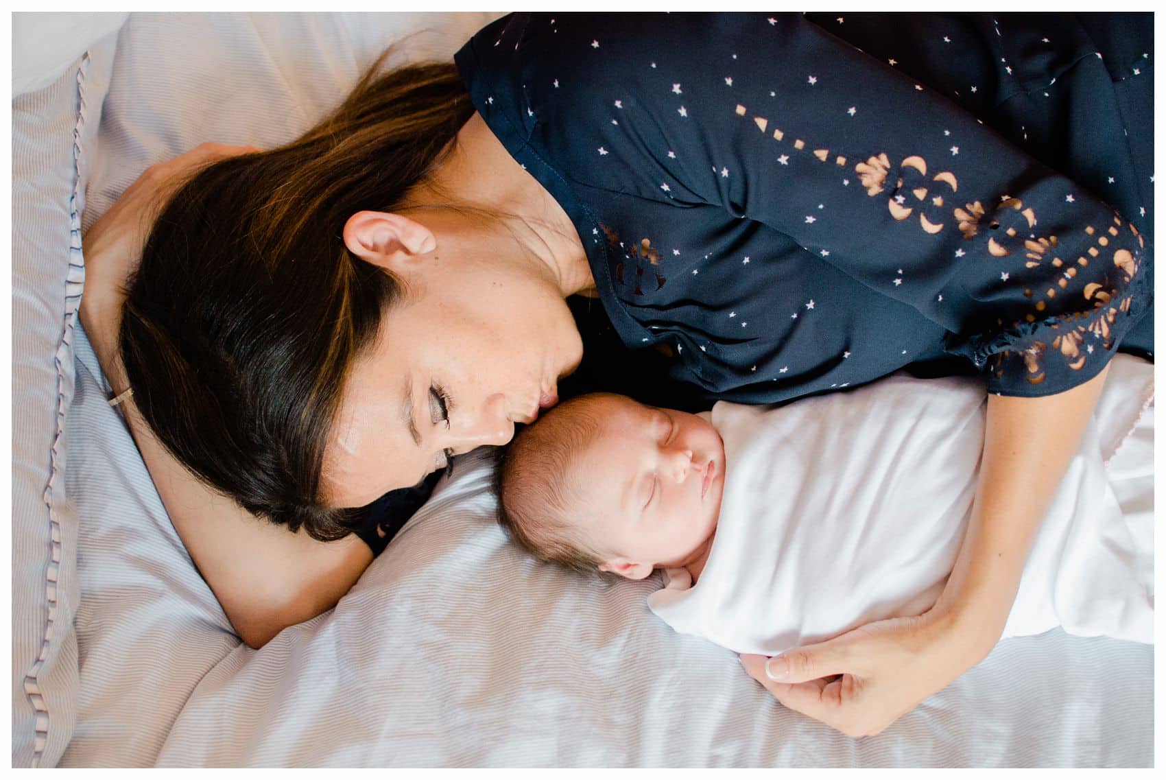 The best newborn photographer is taking a photo of a new mother is kissing her baby girl on bed in NYC 