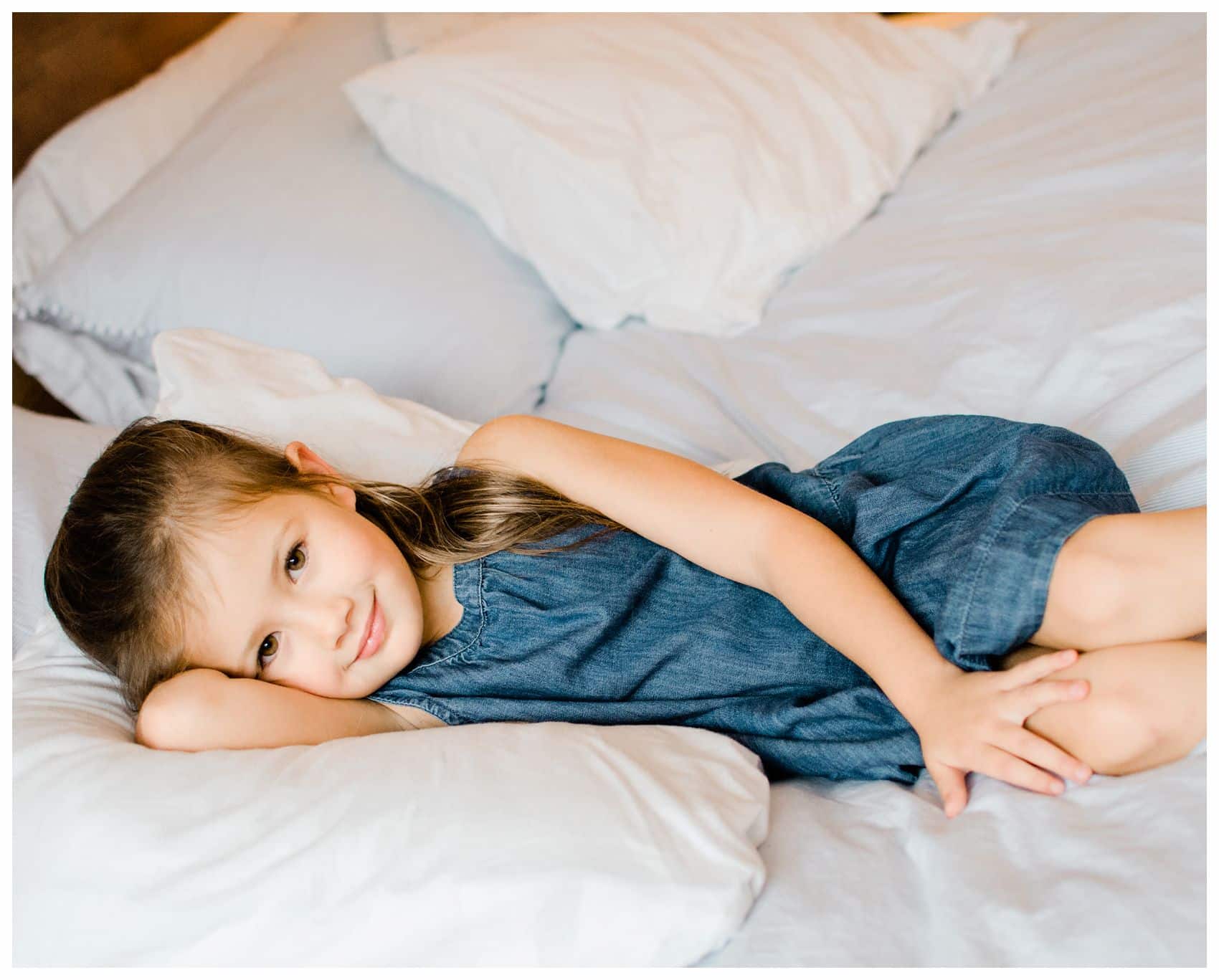 a little girl in denim laying in bed for family photos in NYC