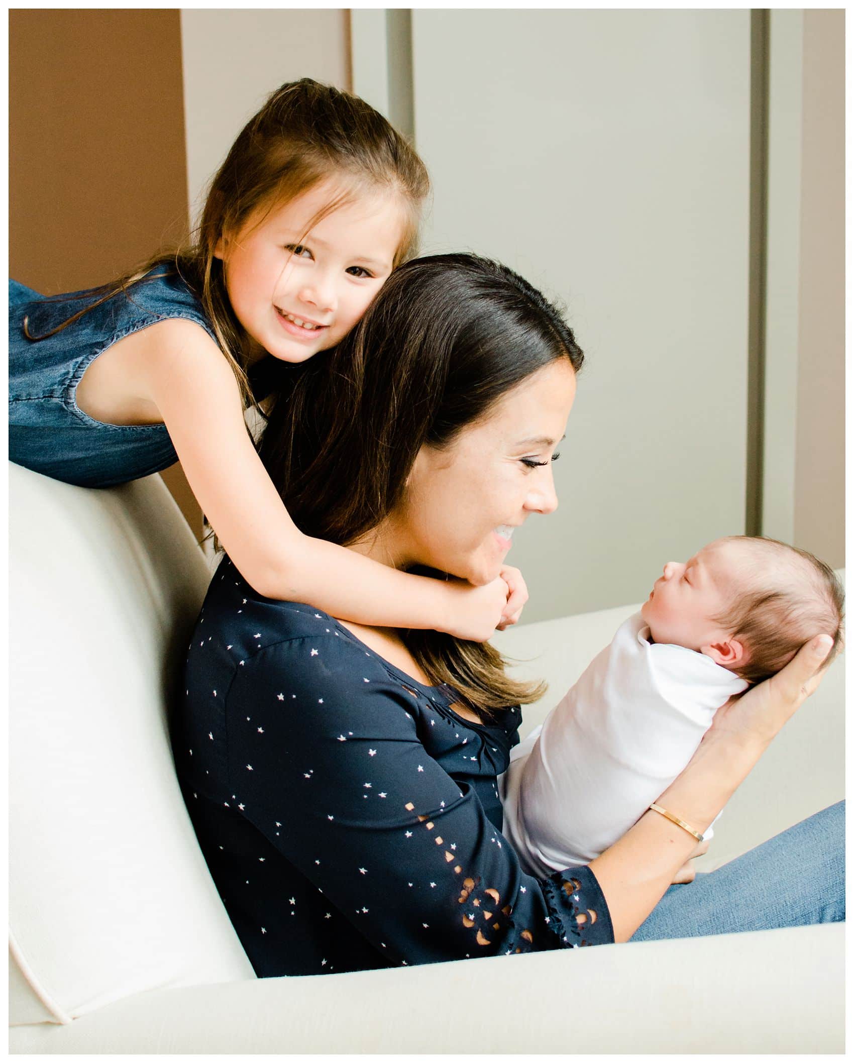 a dither is hugging her smiling mom and newborn baby sister in NYC best newborn photos
