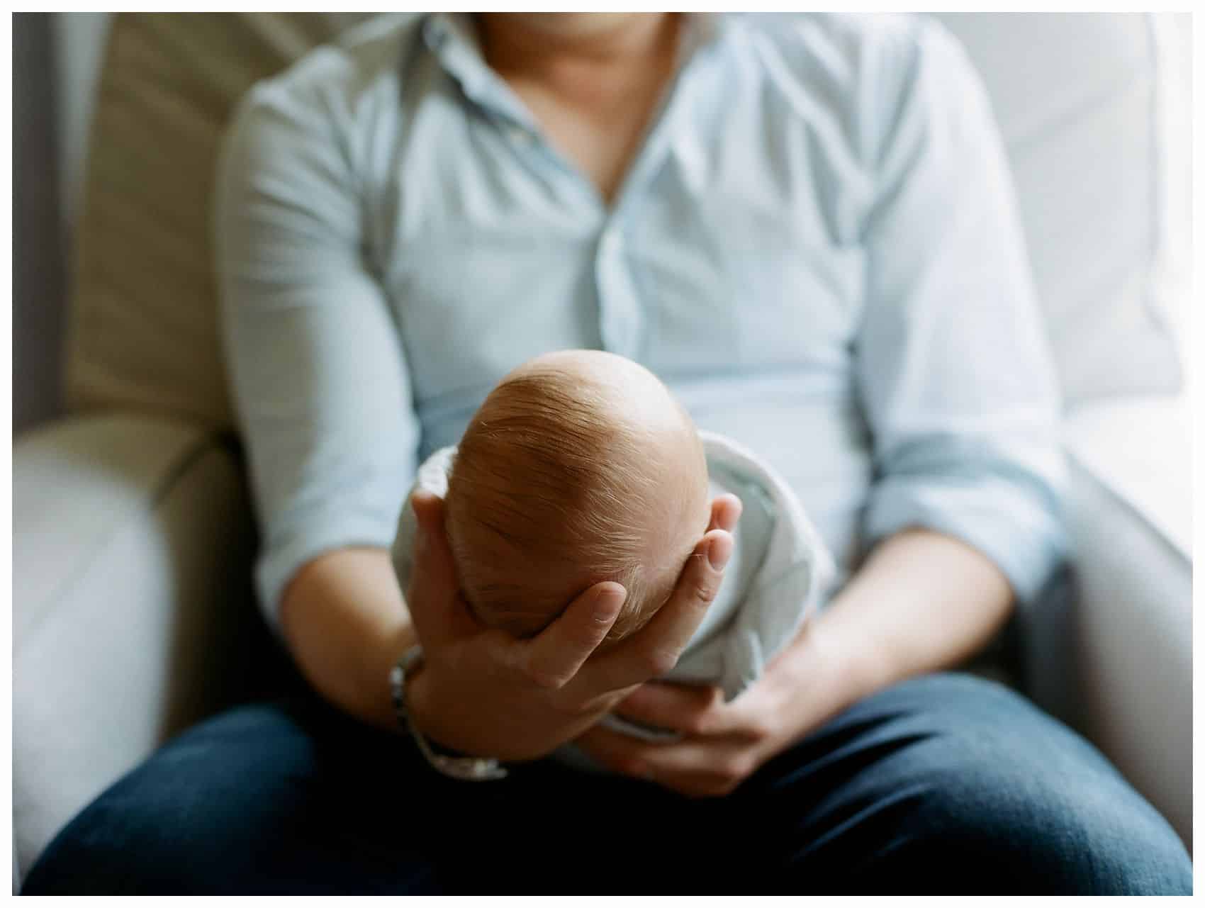 a close up of a little baby held in father's strong arms 