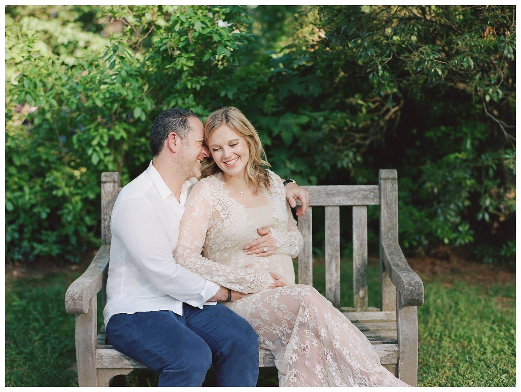pregnant mom in cream lace dress laughing with her husband on a bench during maternity photo session in Essex County NJ