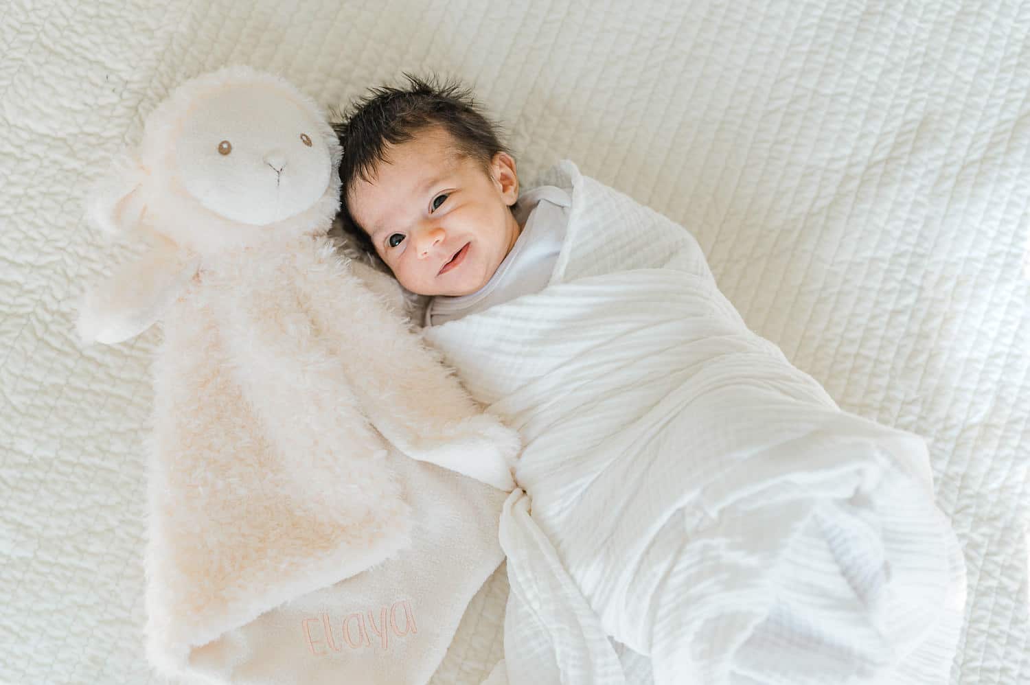 smiling baby girl with her favorite sheep toy during newborn photography NYC session