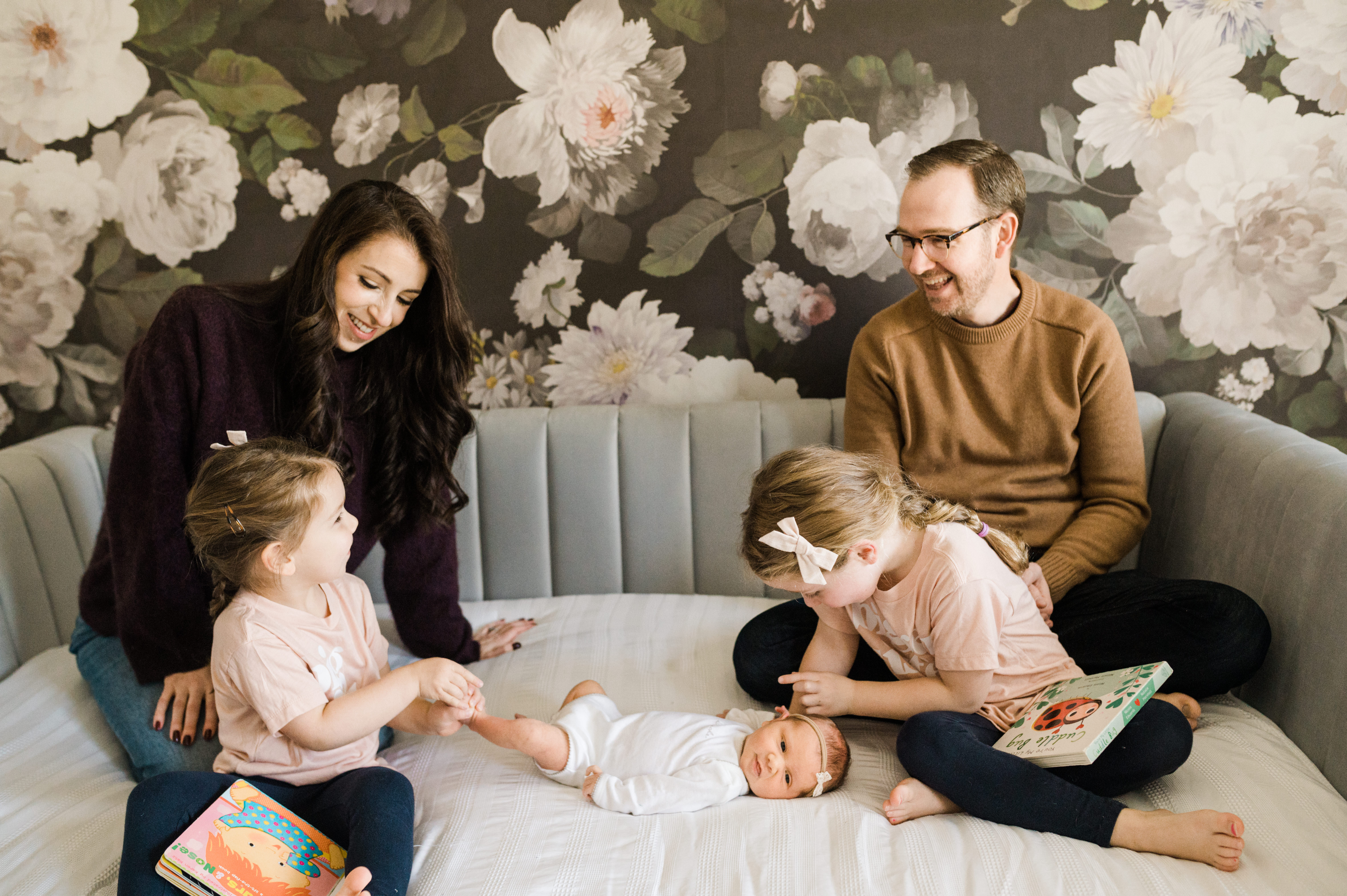 Newborn baby girl being adored by her older two sister and happy parents looking on in their Upper East New York Apartment 