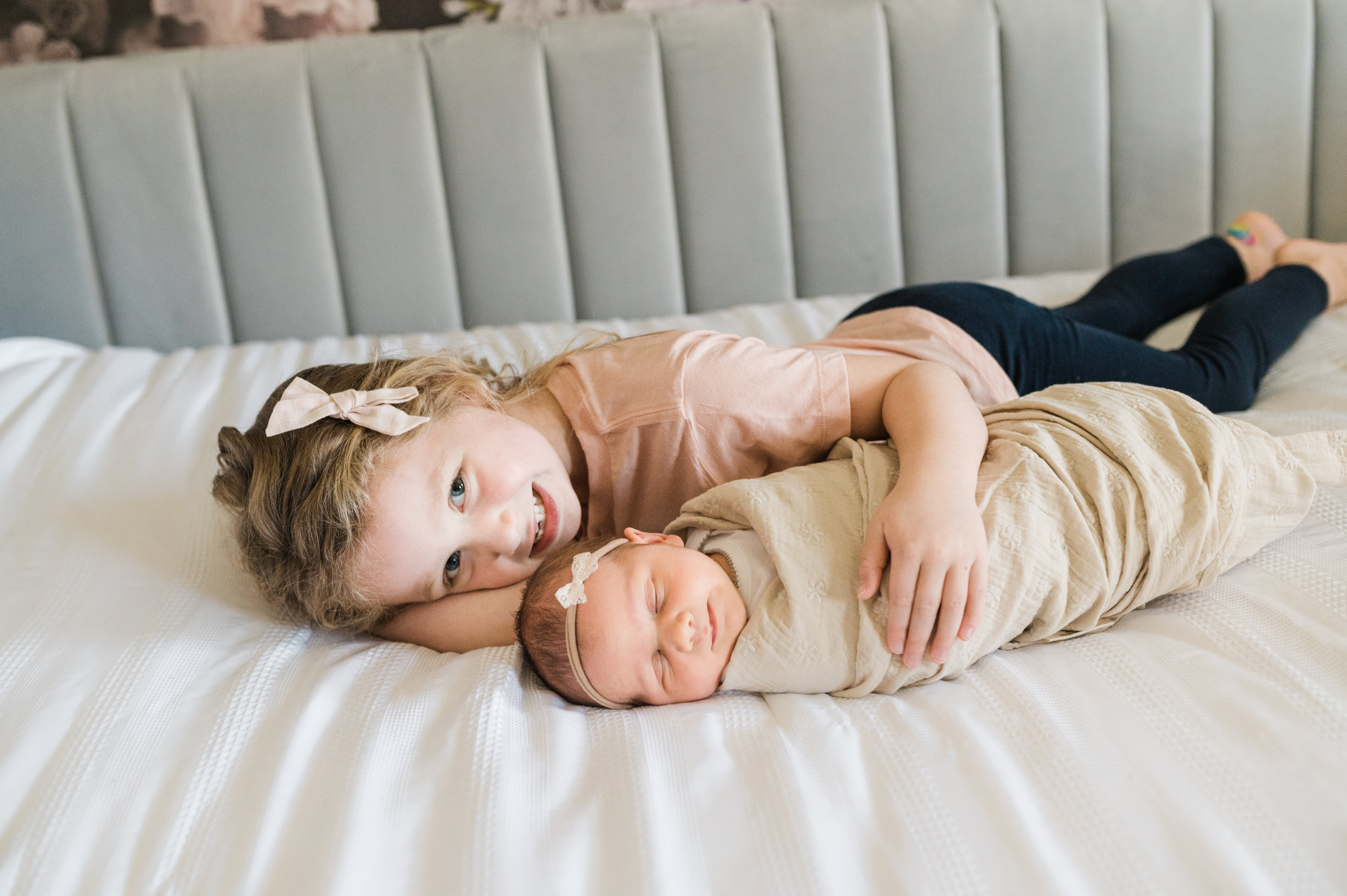 Newborn baby girl lying on a blanket with smiling older sister in their NYC home during newborn photo session 