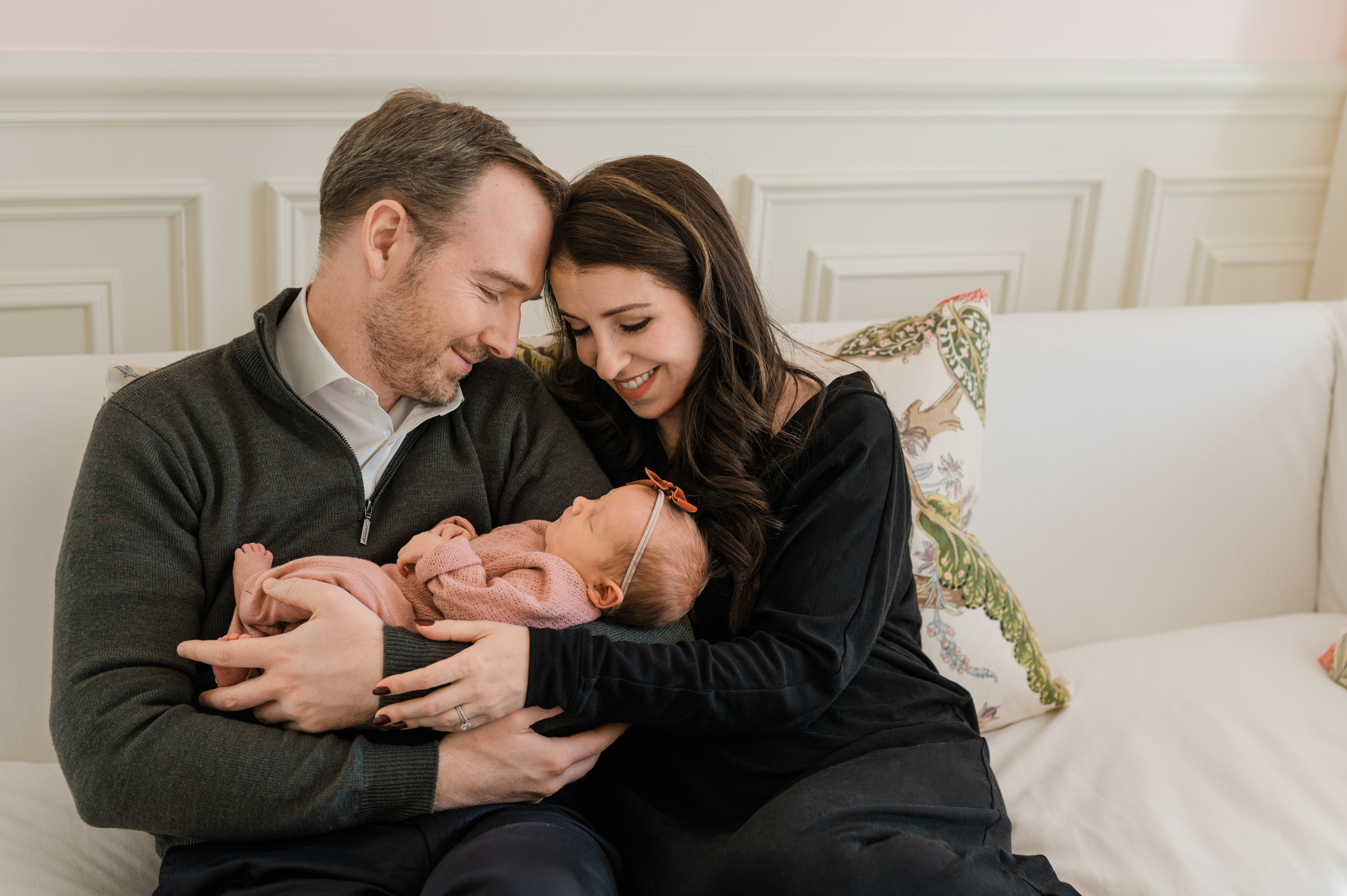 new parents embracing their new baby girl with a bow sitting on the couch in their Manhattan home